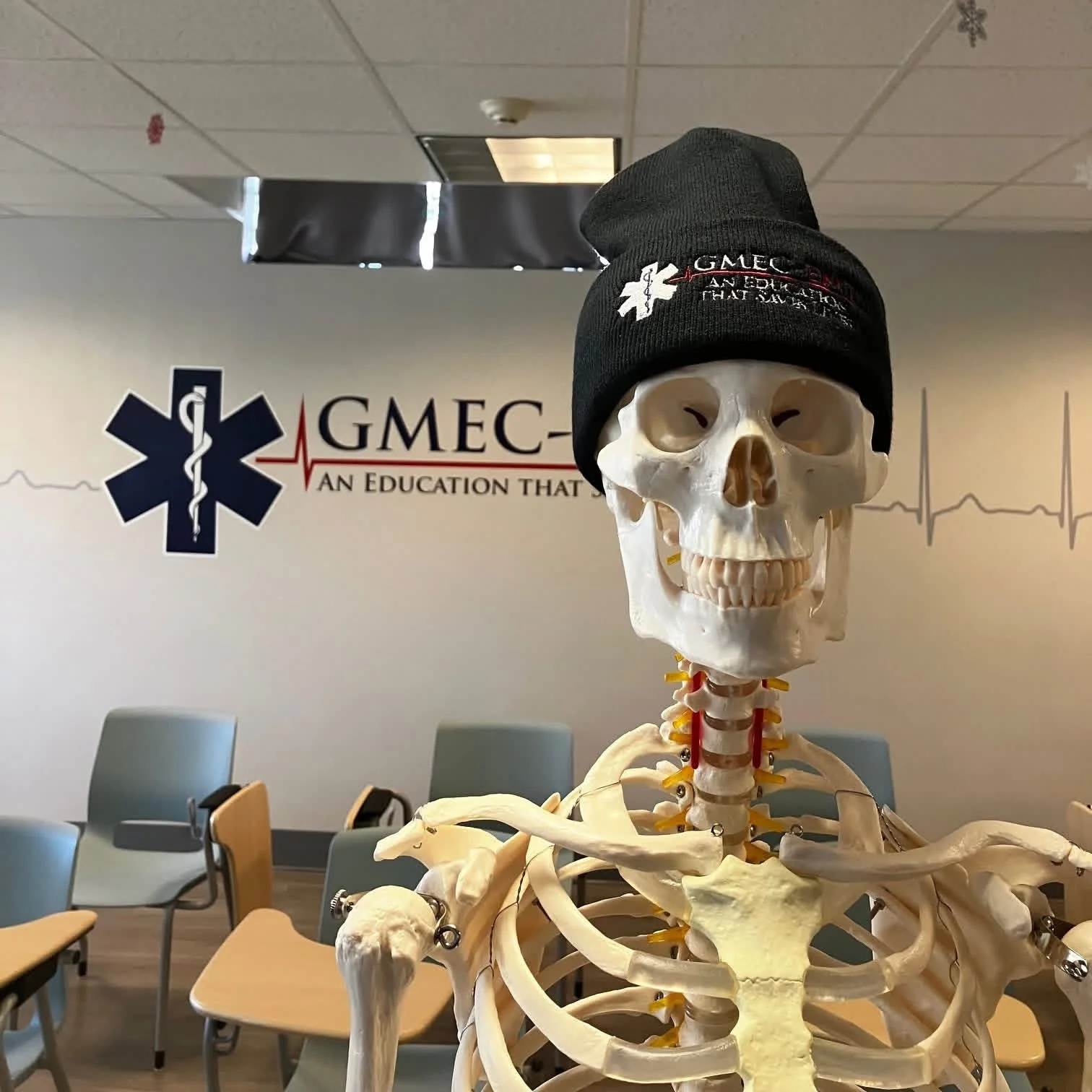 An anatomical teaching skeleton wearing a GMEC hat in the GMEC classroom.