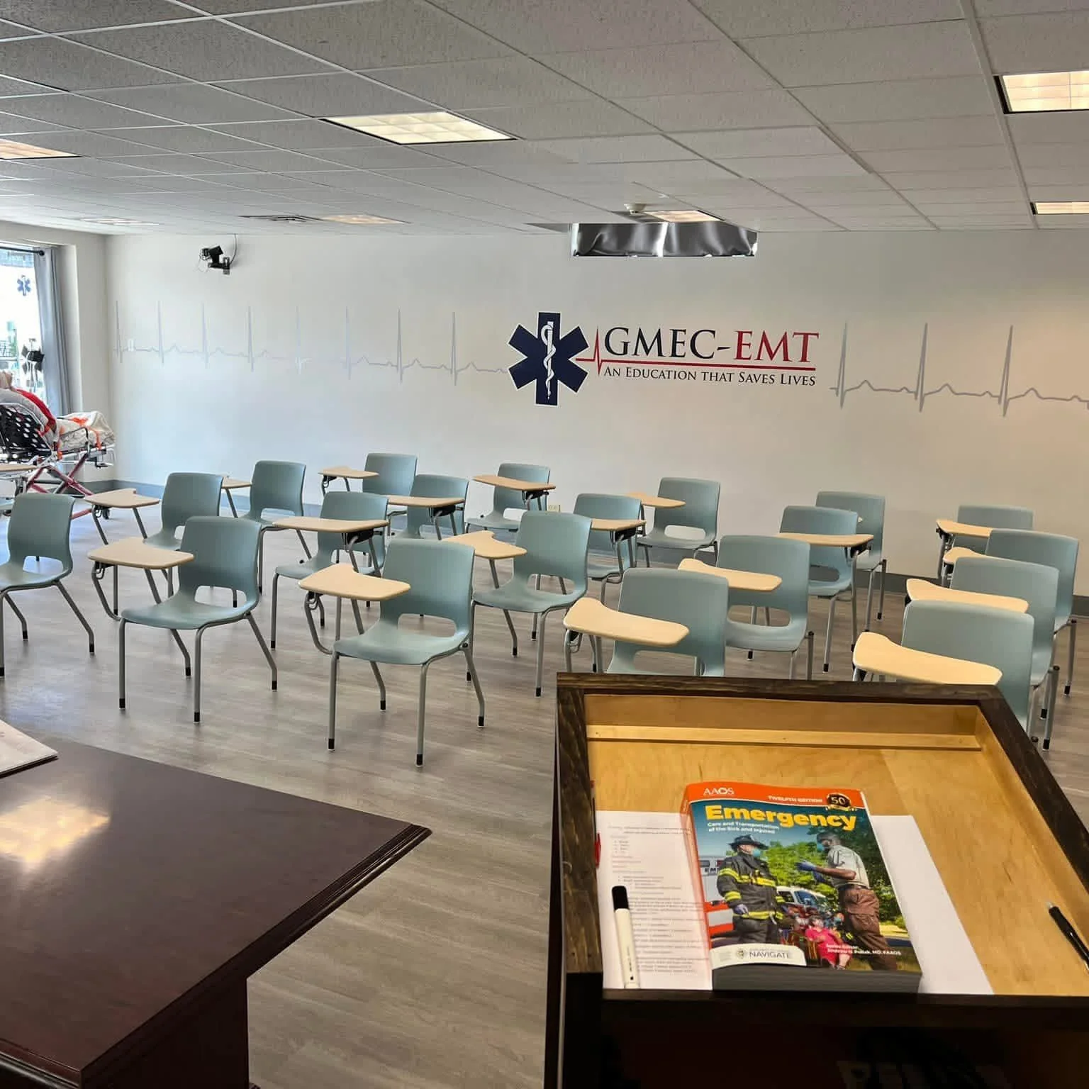 The GMEC-EMT classroom with student desks, wall branding and an emergency care textbook.