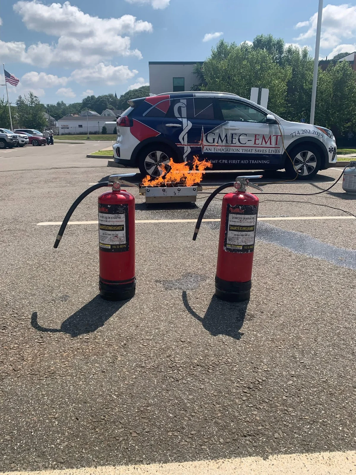 Fire extinguisher training equipment and a controlled practice flame beside the GMEC-EMT vehicle.
