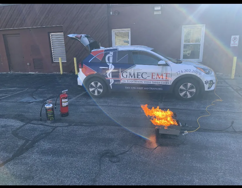 Fire-extinguisher training equipment beside a GMEC-EMT vehicle.