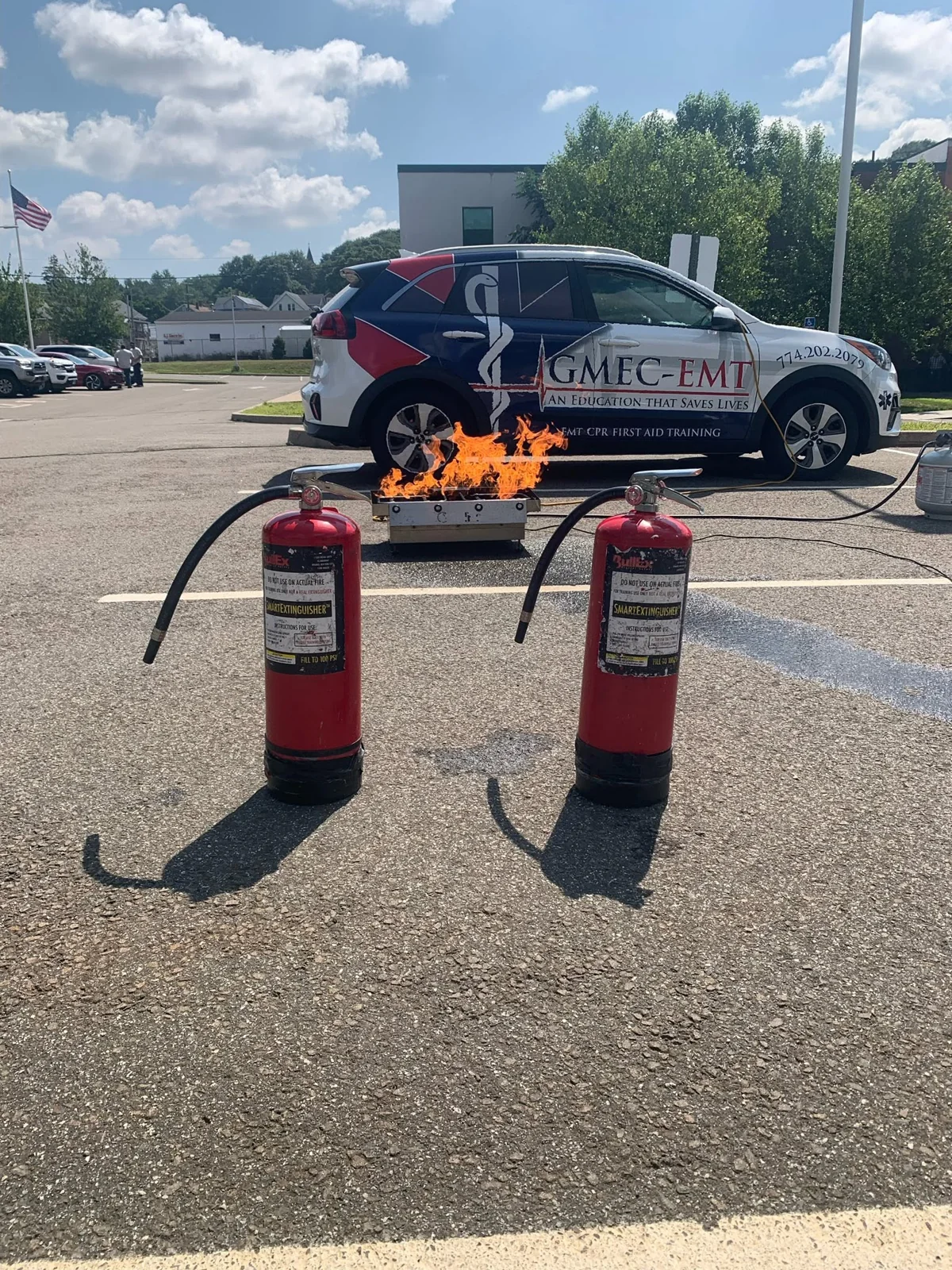 Fire-extinguisher training equipment set up beside a GMEC-EMT vehicle.