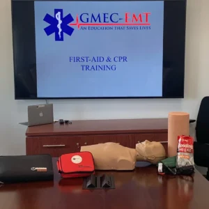 GMEC first-aid and CPR training setup with a manikin, AED trainer and bleeding-control equipment.