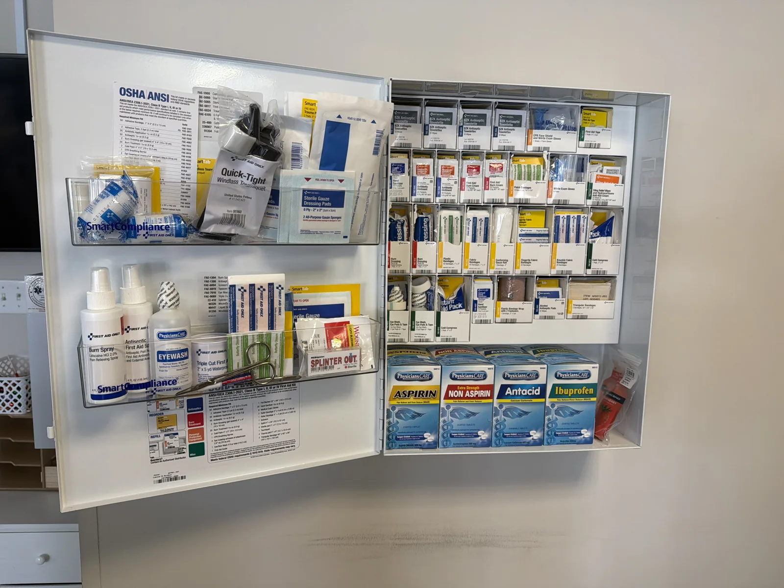 Open workplace first-aid cabinet with organized medical supplies.